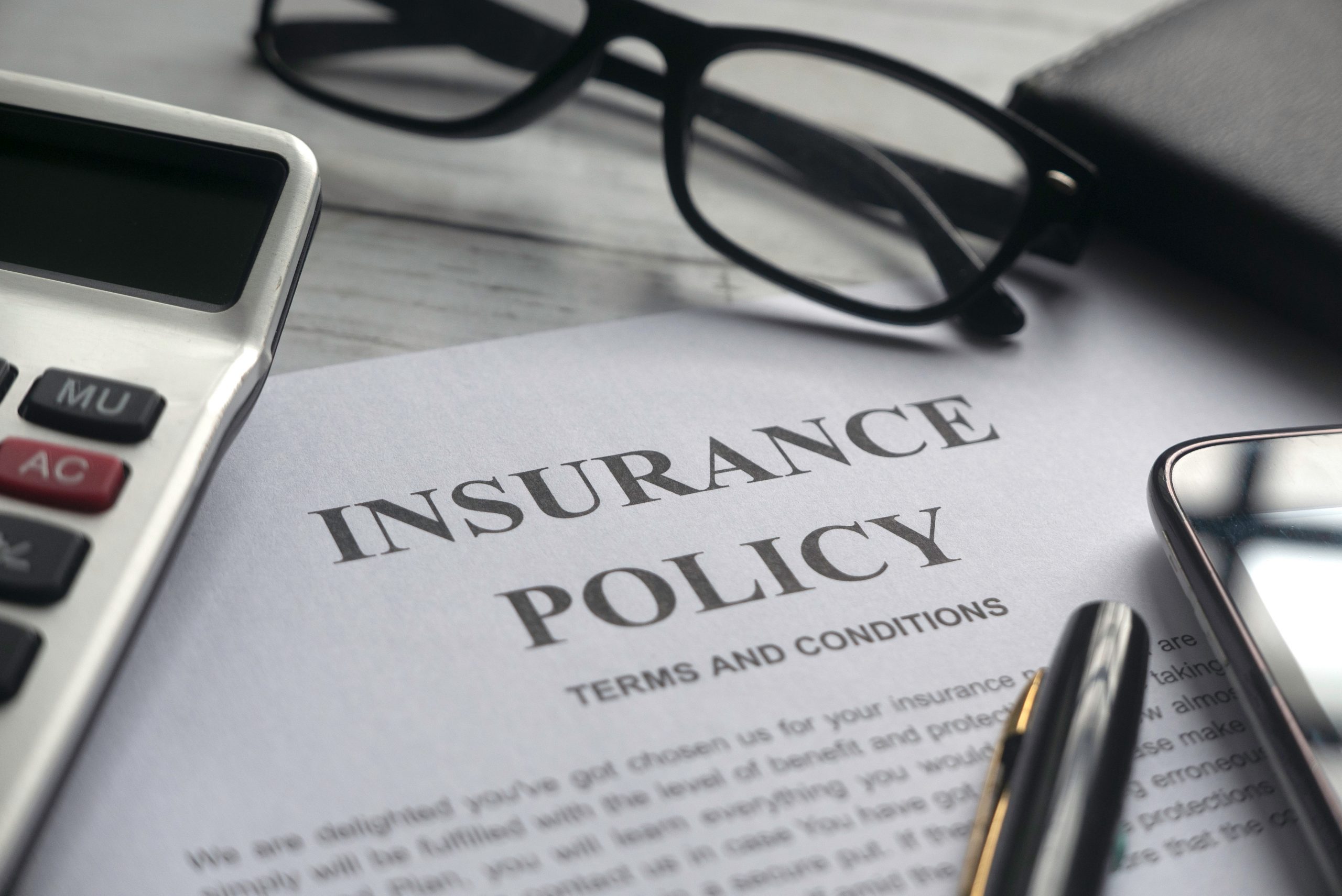  A document with details about insurance policy, along with a calculator, glasses, pen, and mobile phone on a wooden table.